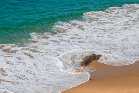 Sea foam forms a \"C\" shape as it rolls around a rock.の写真素材