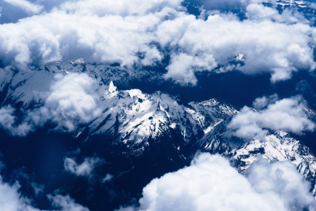 Mountain view from the top through the clouds    The mountain peaks covered with snow  View from...