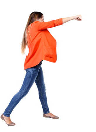 back view of woman funny fights waving his arms and legs. Rear view people collection. backside view of person.  Isolated over white background. girl in a red jacket stands sideways and strike his hand.の写真素材