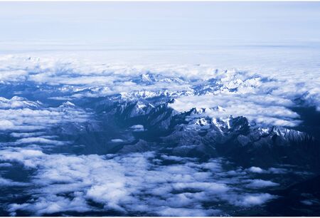 mountain view from an airplane window. top view peaks peeking out of the clouds.