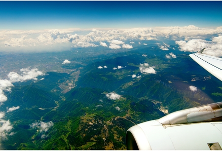 Mountains under the wing of the aircraft. mountain peaks covered with green meadows in the cloudsの写真素材