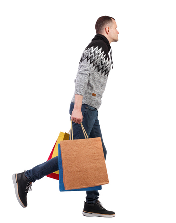 Side view of going man with shopping bags. guy in motion. backside view of person. Rear view people collection. Isolated over white background. The guy in the warm sweater is shopping.の写真素材