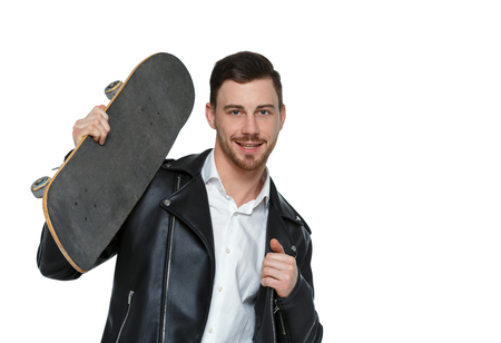 A man with a skateboard. A guy in stylish clothes and trousers posing with a board for skating. Front view. Isolated on white background. Collection of sports people. Stylish guy in a leather jacket posing with a skate on his shoulder.の写真素材