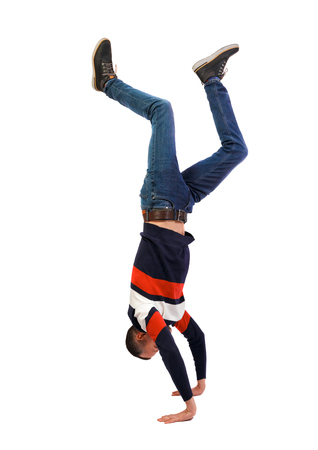 Side view of a man standing on his hands. Stylish guy in a sweater and jeans makes a handstand. backside view of person. Isolated over white background.の写真素材