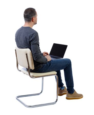 Back view of a man who sits on a chair with a laptop. Rear view people collection. backside view of person. Isolated over white background. A man in a gray jacket sits on a white chair with a laptop looking forward.の写真素材