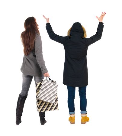 back view of two women with shopping bags  in winter jacket. backside view of person. Rear view people collection. Isolated over white background. Two girls with bags stand next procurement.の写真素材