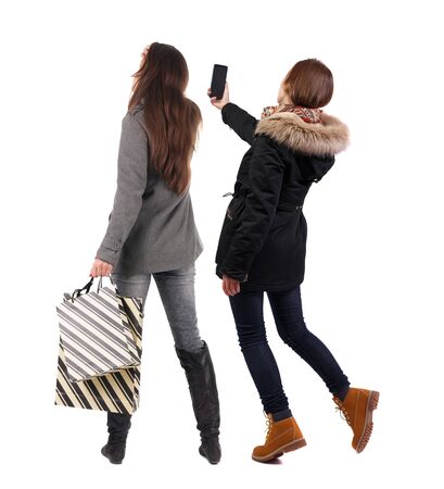 back view of two women with shopping bags  in winter jacket. backside view of person. Rear view people collection. Isolated over white background. Two girls with bags stand next procurement.の写真素材