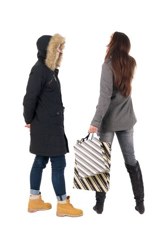 back view of two women with shopping bags  in winter jacket. backside view of person. Rear view people collection. Isolated over white background. Two girls with bags stand next procurement.の写真素材