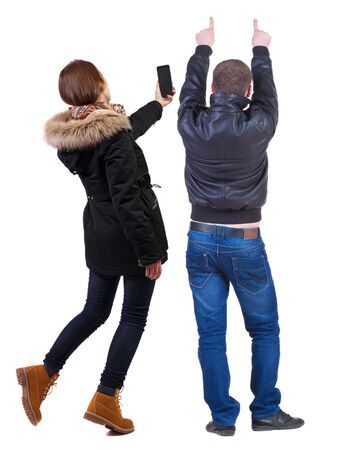 Back view of couple in winter jacket photographed on a mobile phone in winter jacket. beautiful friendly girl and guy together. Rear view people collection. backside view of person. Isolated over white background.の写真素材