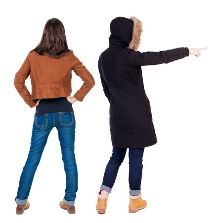 Back view of two pointing young girl in winter jacket. Rear view people collection. backside view of person. beautiful woman friends showing gesture. Rear view. Isolated over white background.の写真素材