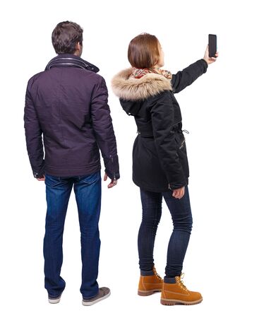 Back view of couple in winter jacket photographed on a mobile phone in winter jacket. beautiful friendly girl and guy together. Rear view people collection. backside view of person. Isolated over white background.の写真素材