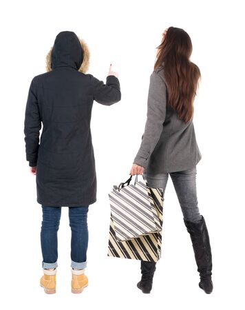 back view of two women with shopping bags in winter jacket. backside view of person. Rear view people collection. Isolated over white background. Two girls with bags stand next procurement.の写真素材