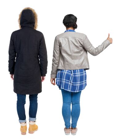Back view of two young girl in winter jacket showing thumb up. Rear view people collection. backside view of person. beautiful woman friends showing gesture. Rear view. Isolated over white background.の写真素材
