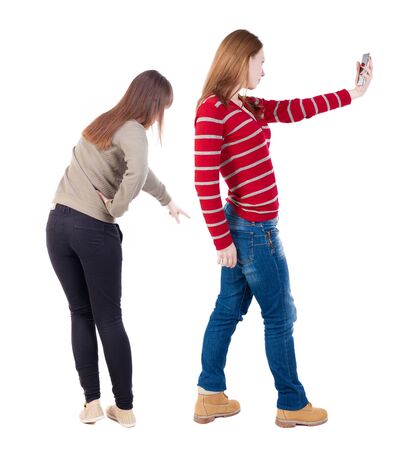 Back view of two young woman photographed on a mobile phone in sweater. Rear view people collection. backside view of person. Rear view. Isolated over white background.の写真素材