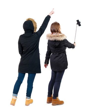 Back view of two young woman photographed on a mobile phone in winter jacket. Rear view people collection. backside view of person. Rear view. Isolated over white background.の写真素材