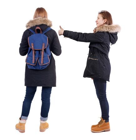 Back view of two young girl in winter jacket showing thumb up. Rear view people collection. backside view of person. beautiful woman friends showing gesture. Rear view. Isolated over white background.の写真素材