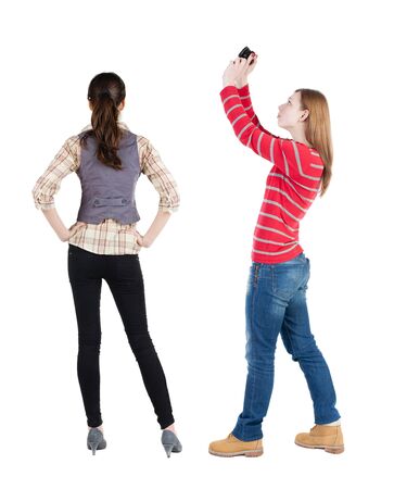 Back view of two young woman photographed on a mobile phone in sweater. Rear view people collection. backside view of person. Rear view. Isolated over white background.の写真素材