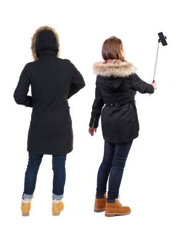 Back view of two young woman photographed on a mobile phone in winter jacket. Rear view people collection. backside view of person. Rear view. Isolated over white background.の写真素材