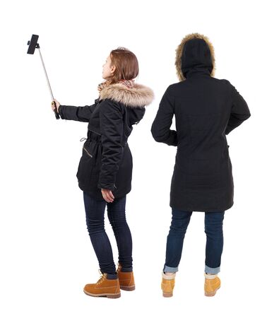 Back view of two young woman photographed on a mobile phone in winter jacket. Rear view people collection. backside view of person. Rear view. Isolated over white background.の写真素材