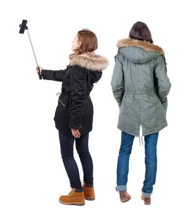 Back view of two young woman photographed on a mobile phone in winter jacket. Rear view people collection. backside view of person. Rear view. Isolated over white background.の写真素材