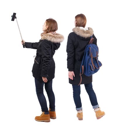 Back view of two young woman photographed on a mobile phone in winter jacket. Rear view people collection. backside view of person. Rear view. Isolated over white background.の写真素材