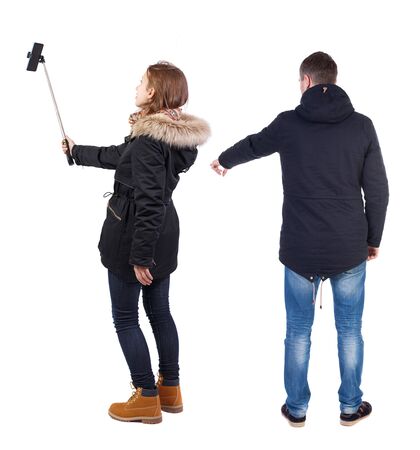 Back view of couple in winter jacket photographed on a mobile phone in winter jacket. beautiful friendly girl and guy together. Rear view people collection. backside view of person. Isolated over white background.の写真素材