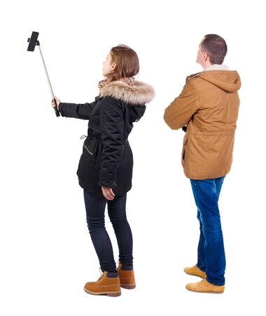 Back view of couple in winter jacket photographed on a mobile phone in winter jacket. beautiful friendly girl and guy together. Rear view people collection. backside view of person. Isolated over white background.の写真素材