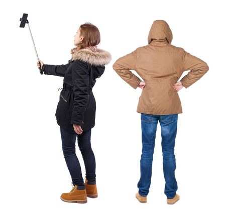 Back view of couple in winter jacket photographed on a mobile phone in winter jacket. beautiful friendly girl and guy together. Rear view people collection. backside view of person. Isolated over white background.の写真素材