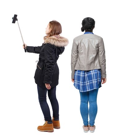 Back view of two young woman photographed on a mobile phone in winter jacket. Rear view people collection. backside view of person. Rear view. Isolated over white background.の写真素材