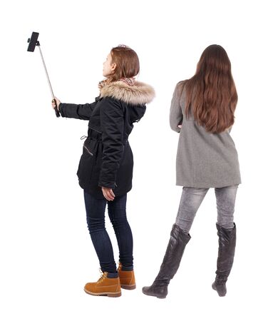 Back view of two young woman photographed on a mobile phone in winter jacket. Rear view people collection. backside view of person. Rear view. Isolated over white background.の写真素材