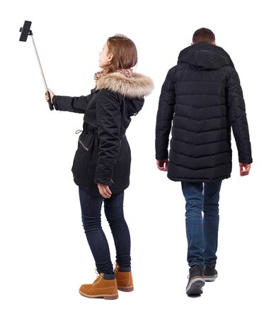 Back view of couple in winter jacket photographed on a mobile phone in winter jacket. beautiful friendly girl and guy together. Rear view people collection. backside view of person. Isolated over white background.の写真素材