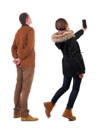 Back view of couple in winter jacket photographed on a mobile phone in winter jacket. beautiful friendly girl and guy together. Rear view people collection. backside view of person. Isolated over white background.の写真素材