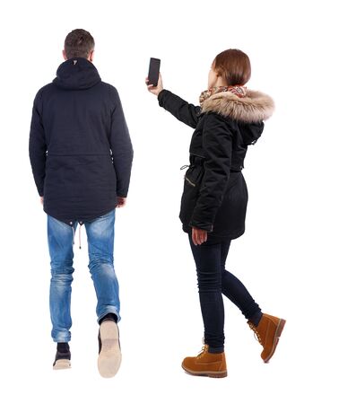Back view of couple in winter jacket photographed on a mobile phone in winter jacket. beautiful friendly girl and guy together. Rear view people collection. backside view of person. Isolated over white background.の写真素材