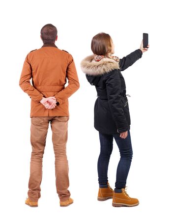 Back view of couple in winter jacket photographed on a mobile phone in winter jacket. beautiful friendly girl and guy together. Rear view people collection. backside view of person. Isolated over white background.の写真素材