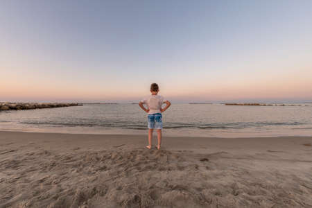 Child standing on the seashore at sunset looking at the horizon