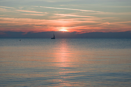 Sunset over the sea with a sailboat on the horizon.の写真素材