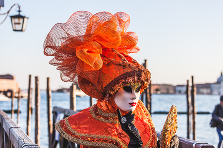 VENICE, ITALY - FEBRUARY 10 2018: Close up of orange dressed carnival mask adorned with fantasy motifs. The masks are photographed with the background of the Giudecca canalのeditorial素材