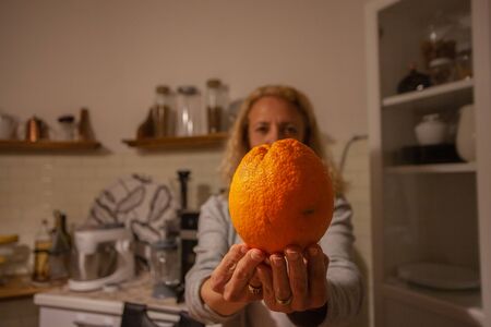 female holding an orange with a kitchen in the backgroundの写真素材