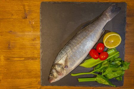 Slate dish with sea bass, lemon, celery and tomatoes. Concept: cuisine based on fish