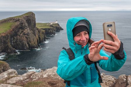 Chilled woman taking photo on a rainy day with cliffs of Neist Point behind herの写真素材