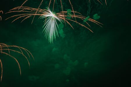 Orange, green and white fireworks against the backdrop of the night sky