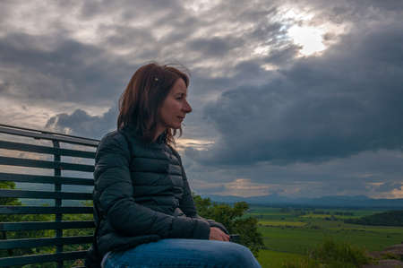 Girl sitting on a bench while contemplating thoughtfully the landscape in a cloudy day. Concept: relax in places with charm and mystery, travel to Scotlandの写真素材