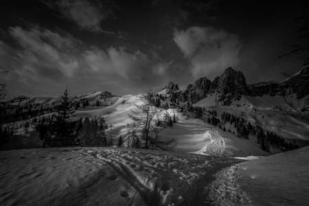 Black and view of path in the snow with human traces that leads to snowy hills