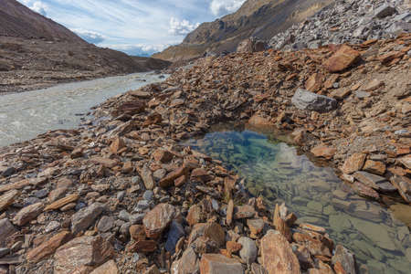 Crystal clear pond, in the middle of moraines near a turbid glacial streamの写真素材