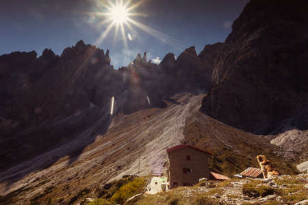 Dog watching alpine hut with dolomite peaks background in Comelico regionの写真素材