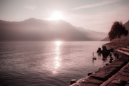 Fantasy pink color effect of sun rising behind the mountains overlooking a lakeの写真素材