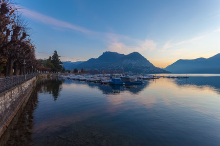 Sunrise panorama of Lugano lake in autumn with mooring for pleasure boatsの写真素材