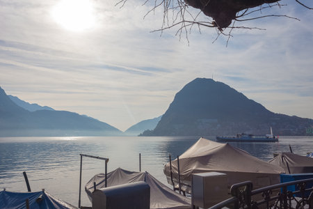 Boat sailing on Lake Lugano at dawn seen from the mooring of pleasure boatsの写真素材