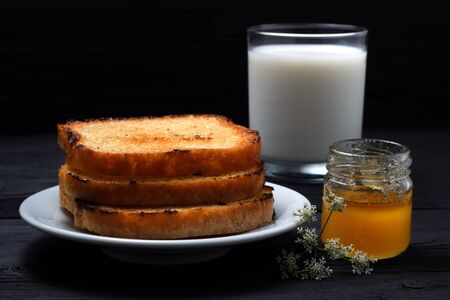 Toast on a plate with milk and a can of honey. On a black wooden backgroundの写真素材