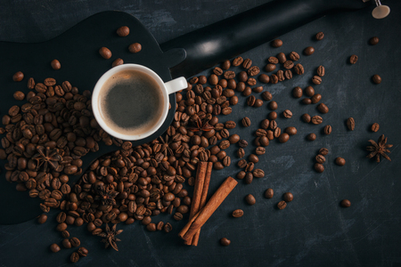 A cup of coffee is on a black ululele with scattered coffee beans, anise and cinnamonの写真素材